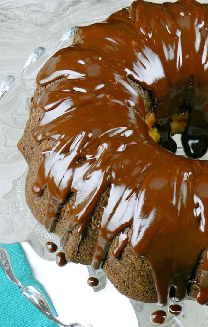 Chocolate Peppermint Cream Cheese Bundt Cake topped with a layer of chocolate ganache sitting on a glass cake plate with a teal napkin
