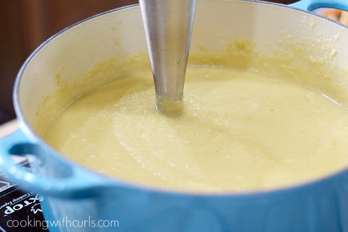 Creamy soup being pureed in a blue Dutch oven with an immersion blender.