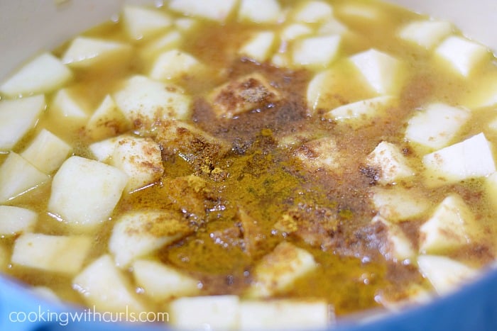 Seasonings sprinkled on top of potato and parsnip chunks floating in broth inside a blue pot.