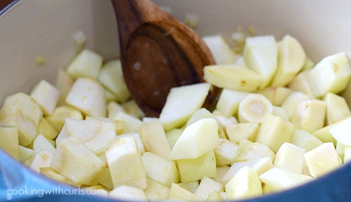 Chopped parsnip and potato with a wooden spoon in a blue pot.