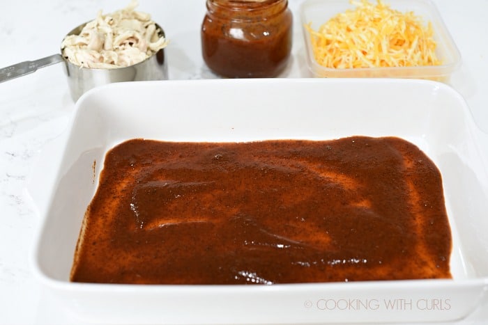 Enchilada sauce spread in the bottom of a baking dish.
