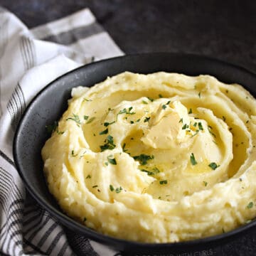 A black bowl filled with fluffy mashed potatoes topped with butter.