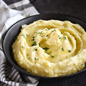 A black bowl filled with creamy mashed potatoes topped with butter.