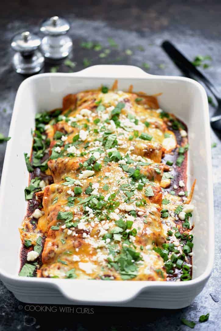 A baking dish filled with enchiladas in red sauce with melted cheese and chopped cilantro.