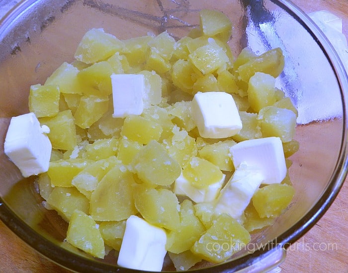 Cooked potato chunks and blogs of butter in a glass mixing bowl