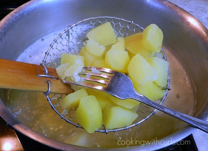 Potato chunks in a strainer being tested with a fork