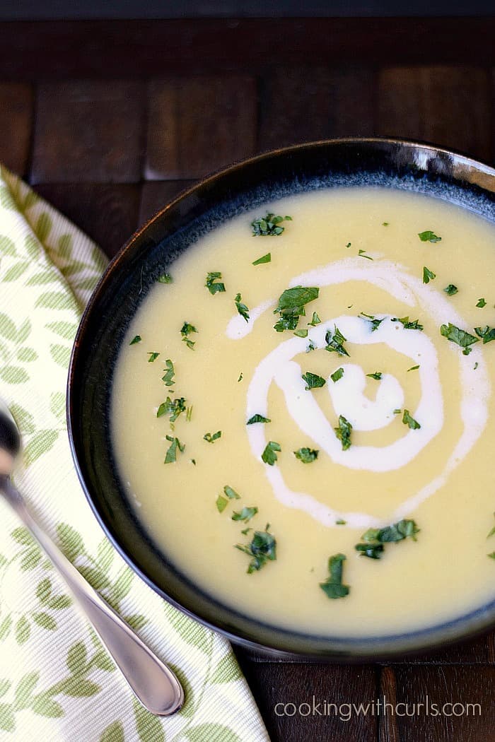 Irish Potato Leek Soup in a dark bowl, sitting on a dark wooden placemat with a leaf motif napkin and spoon on the side