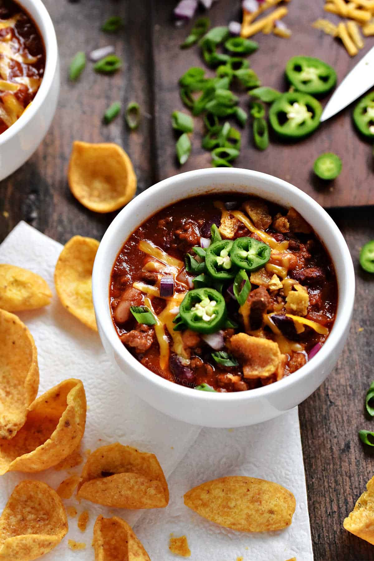 Two bowls of Guinness Beef Chili topped with cheddar cheese, green onions, and sliced jalapeños. 