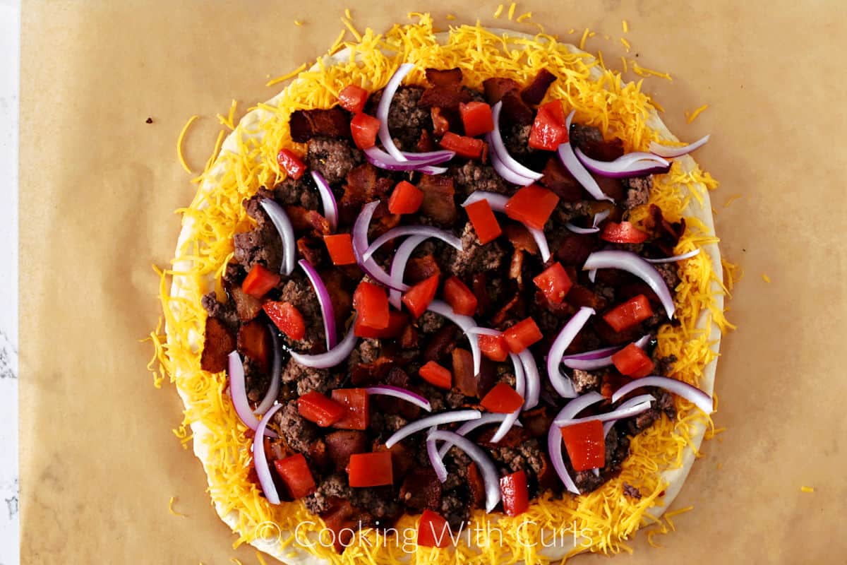 Thin red onion slices and diced tomato on top of the meat on a cheddar cheese edged pizza circle. 