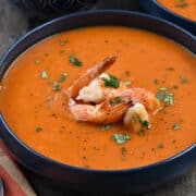 A bowl of roasted red pepper soup topped with large shrimp and sprinkled with chopped cilantro.