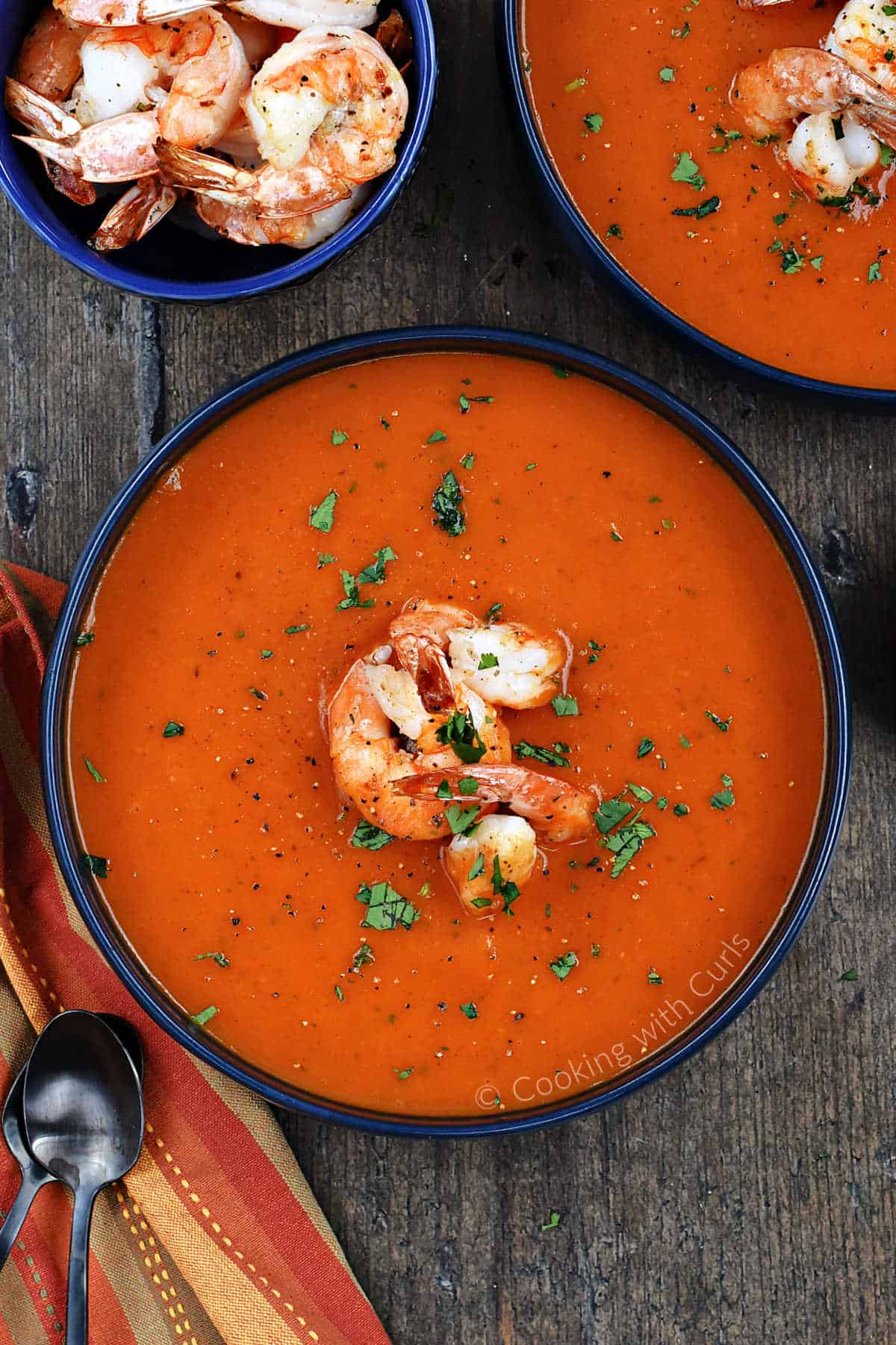 Looking down on two bowls of red pepper soup topped with cooked shrimp and chopped cilantro.