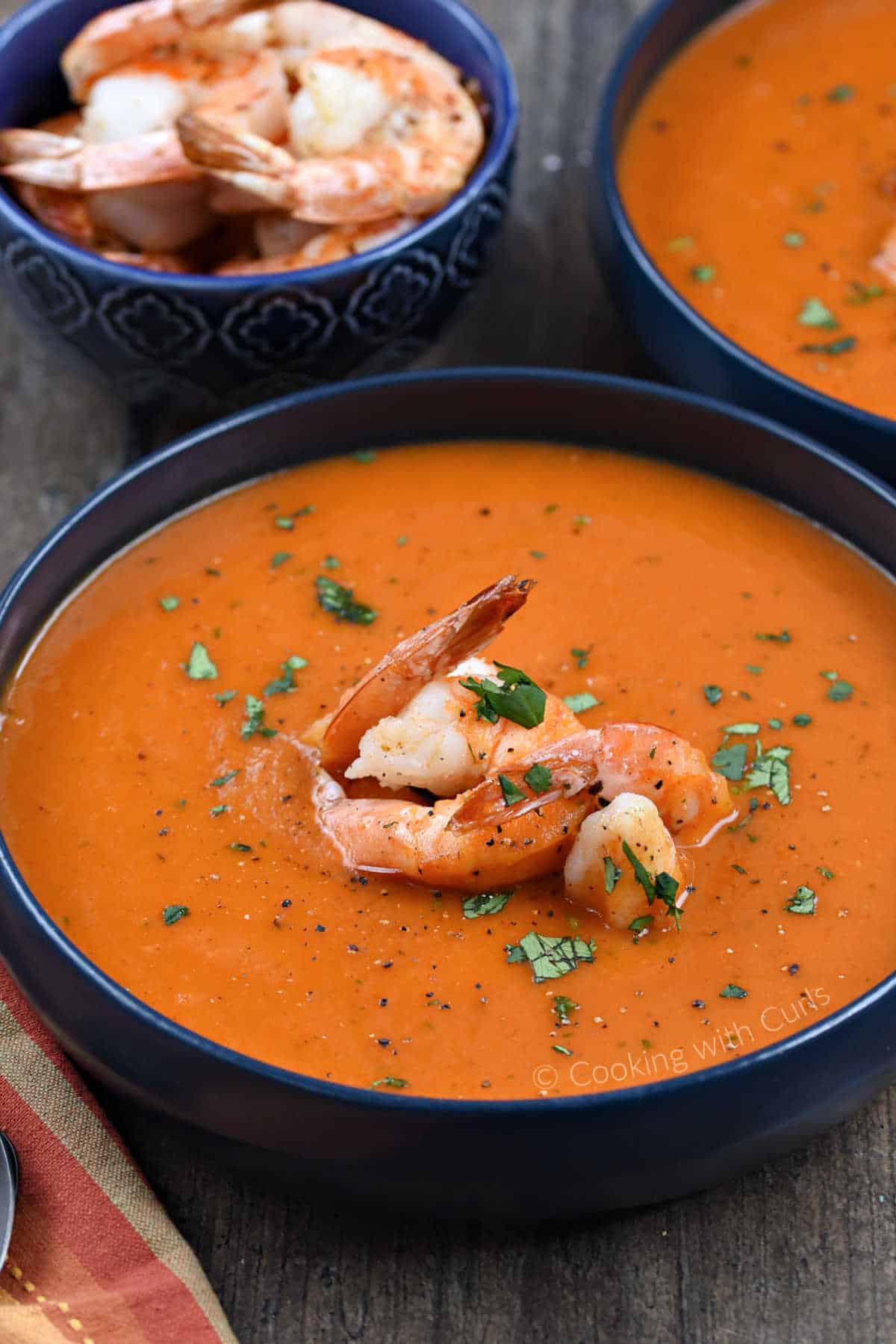 Two bowls of roasted red pepper soup topped with large shrimp and sprinkled with chopped cilantro.