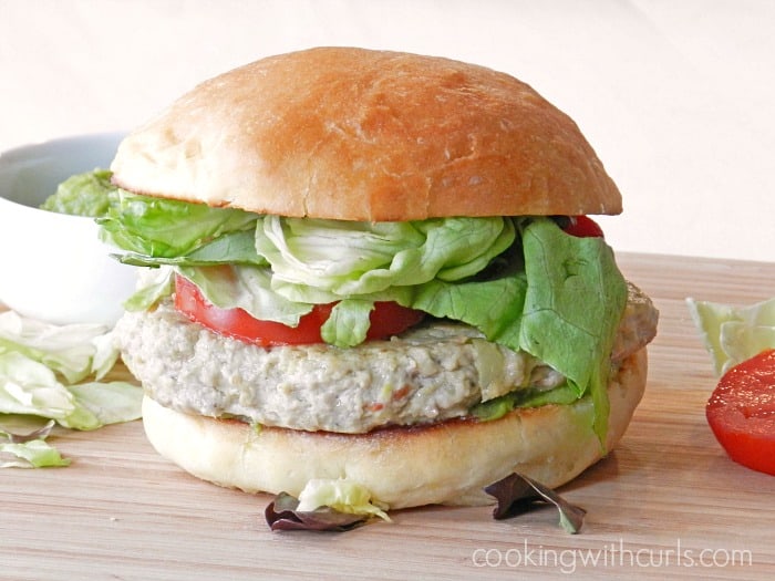 A big, juicy Wholly Guacamole Chicken Burger sitting on a wooden cutting board