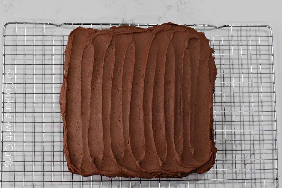Peanut butter chocolate frosting spread over the banana chocolate chip cake sitting on a wire cooling rack.
