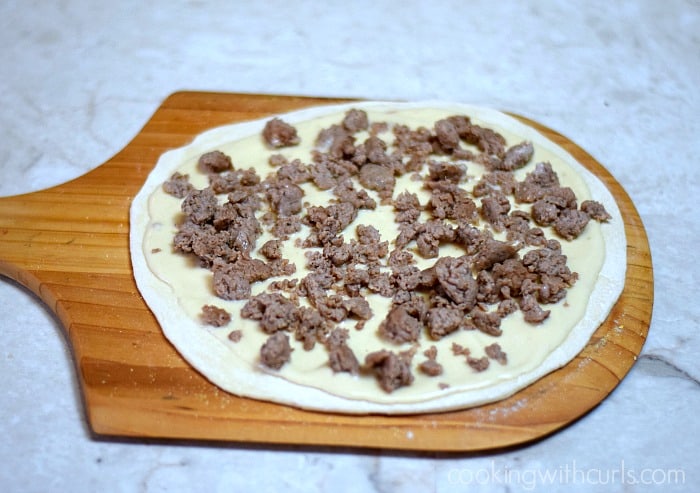 Crumbled sausage over the gravy topped pizza crust on a pizza peel.