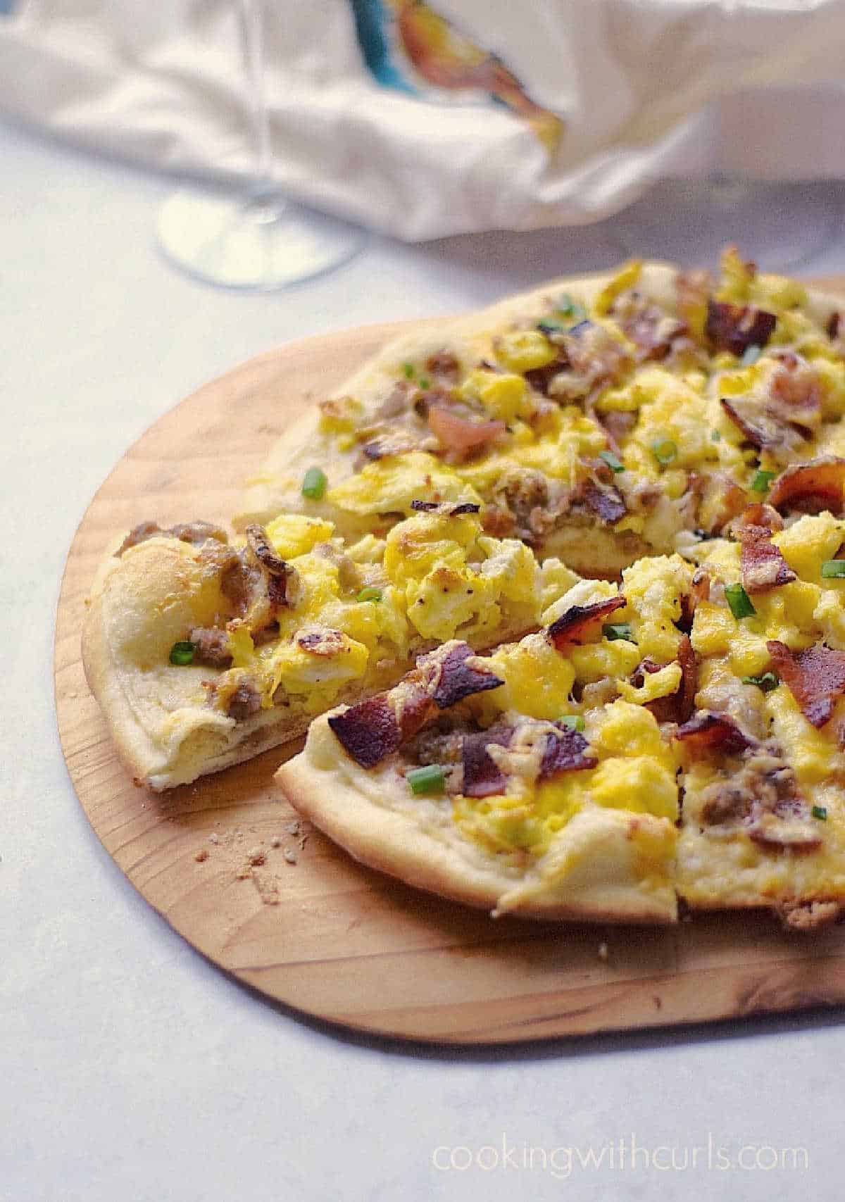 Breakfast Pizza with Sausage Gravy, scrambled eggs, and chopped bacon cut into slices on a wooden pizza peel. 