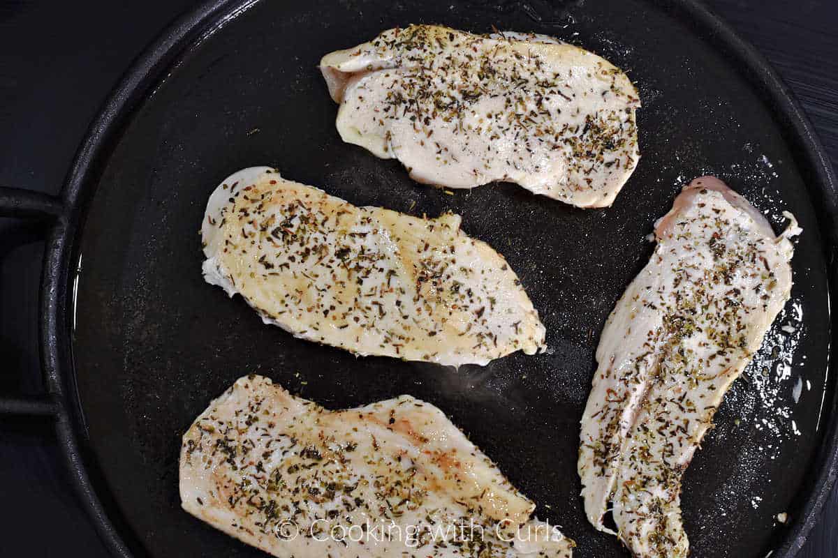 Four seasoned chicken breasts cooking on a cast iron griddle.