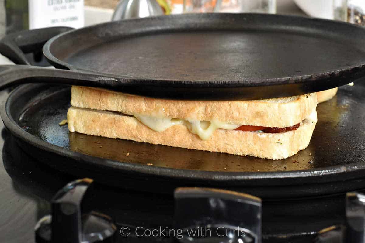 Chicken club sandwich on a cast iron griddle with a cast iron pan on top.