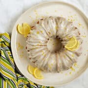 Limoncello glazed bundt cake on a cake plate with lemon zest sprinkled on top and lemon wedges on the sides.