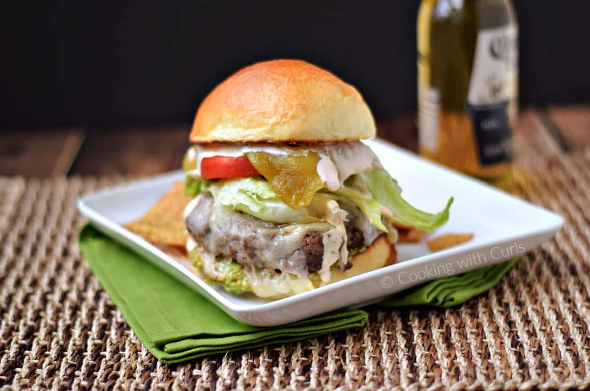 Cheeseburger topped with guacamole, lettuce, tomato, green chiles, and sauce.