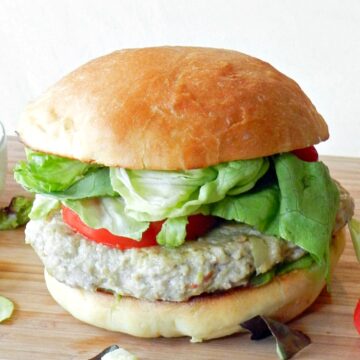 ground chicken burger topped with lettuce and tomato with a fluffy hamburger bun sitting on a wooden cutting board