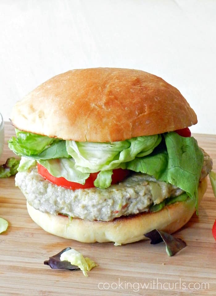 ground chicken burger topped with lettuce and tomato with a fluffy hamburger bun sitting on a wooden cutting board 