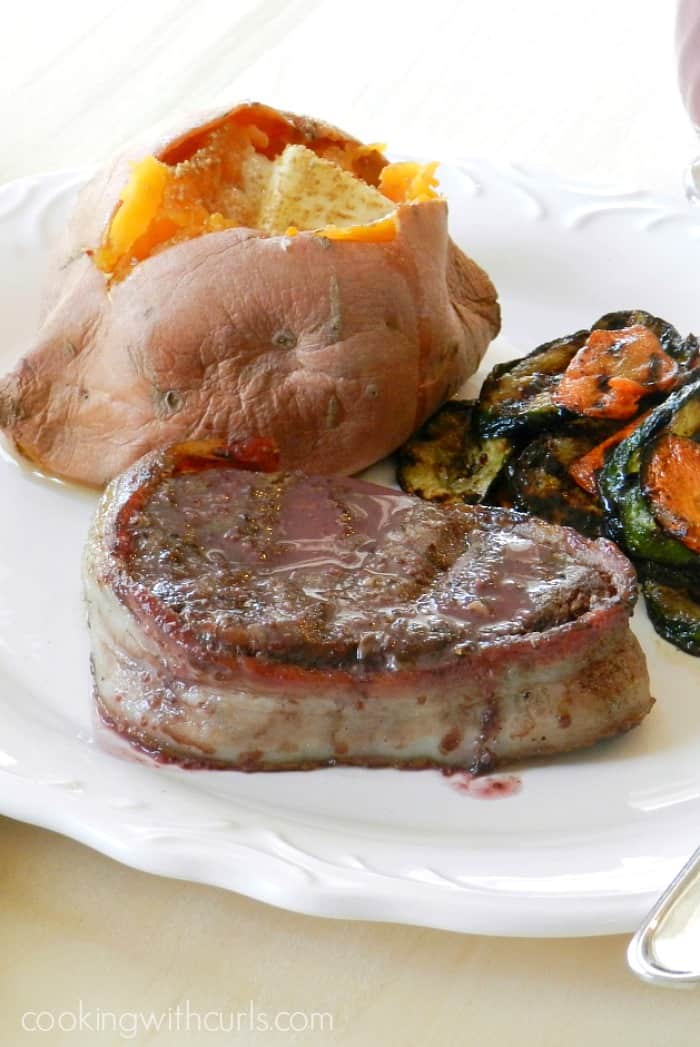 Bacon Wrapped Filet Mignon with Red Wine Sauce, grilled vegetables and a sweet potato on a white plate