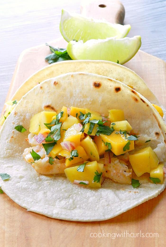 Baked Fish Tacos topped with Papaya Mango Salsa sitting on a wood cutting board