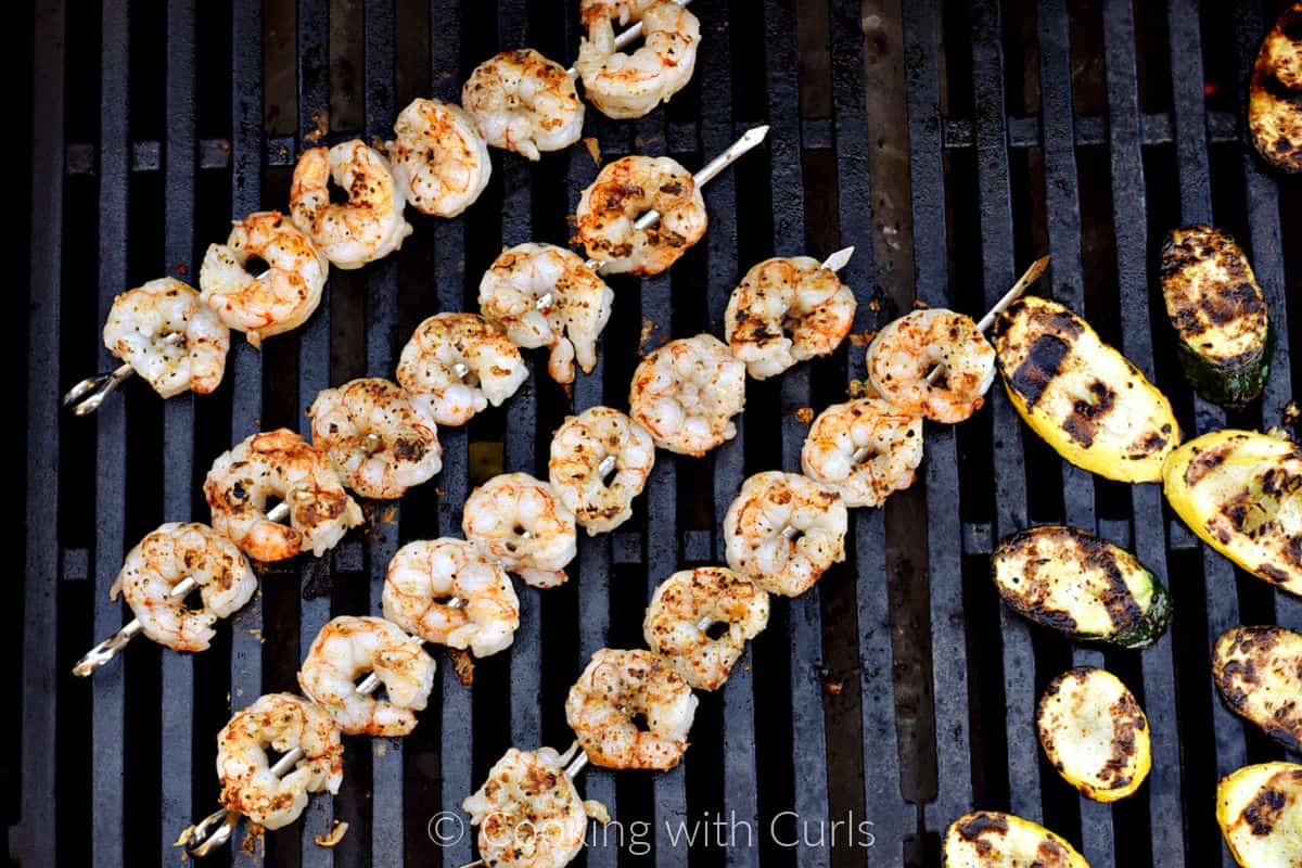 Four skewers of shrimp on the grill with sliced squash. 
