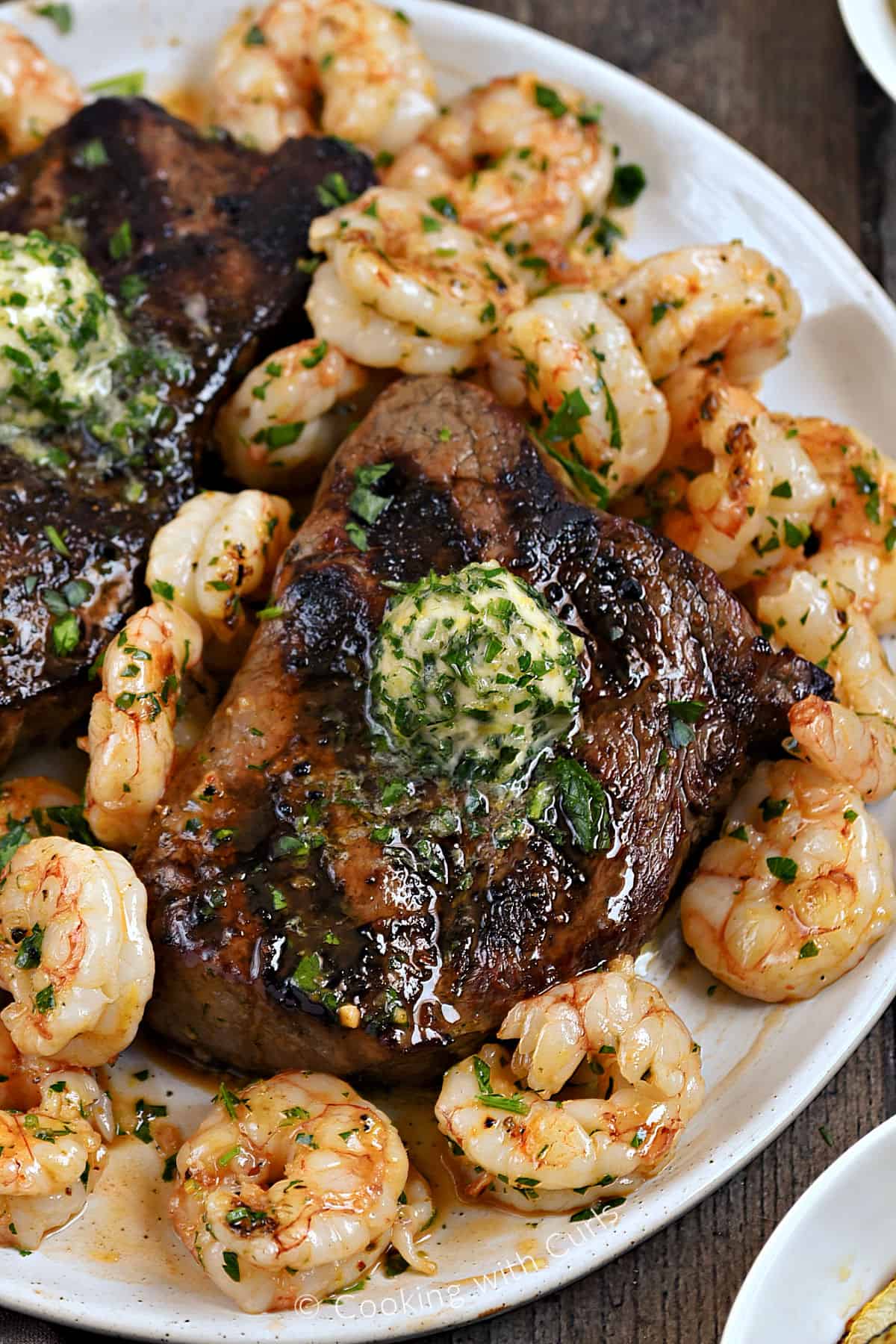 Looking down on a plate of Grilled Steak and Shrimp topped with garlic-lemon butter.