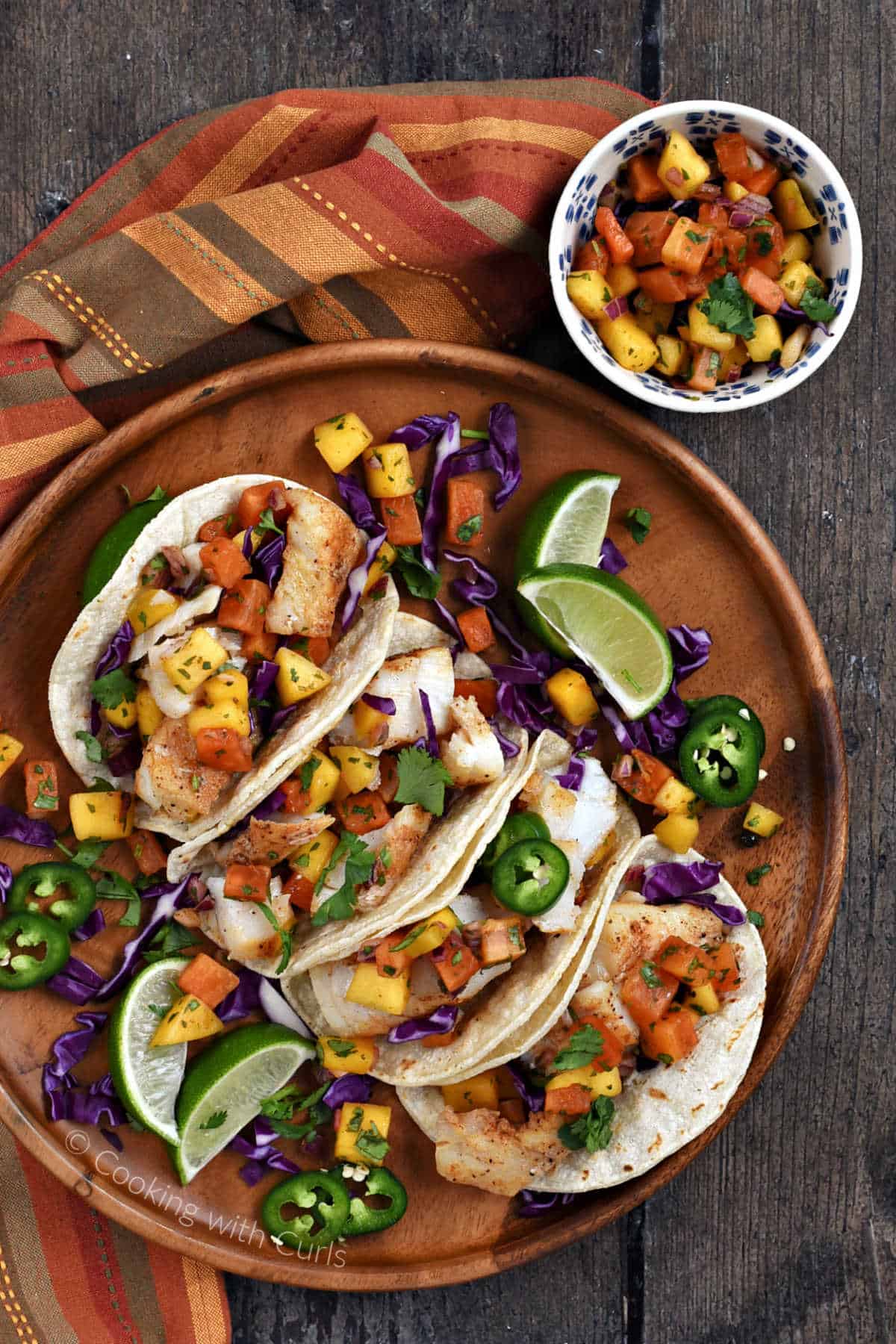 Looking down on four fish tacos with mango salsa and shredded red cabbage on a wood platter.