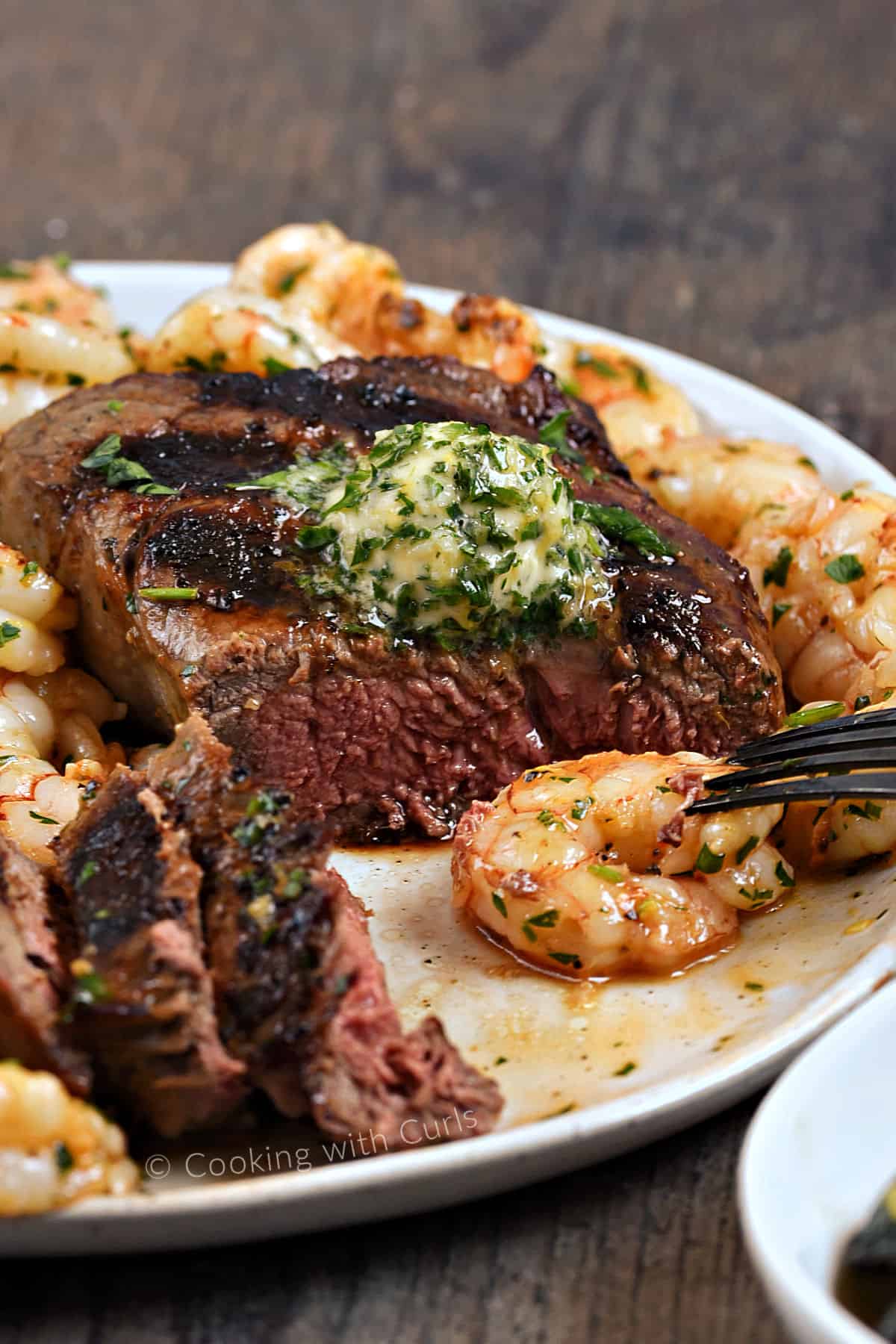 Medium-rare steak topped with lemon herb butter, cut open and surrounded by shrimp. 