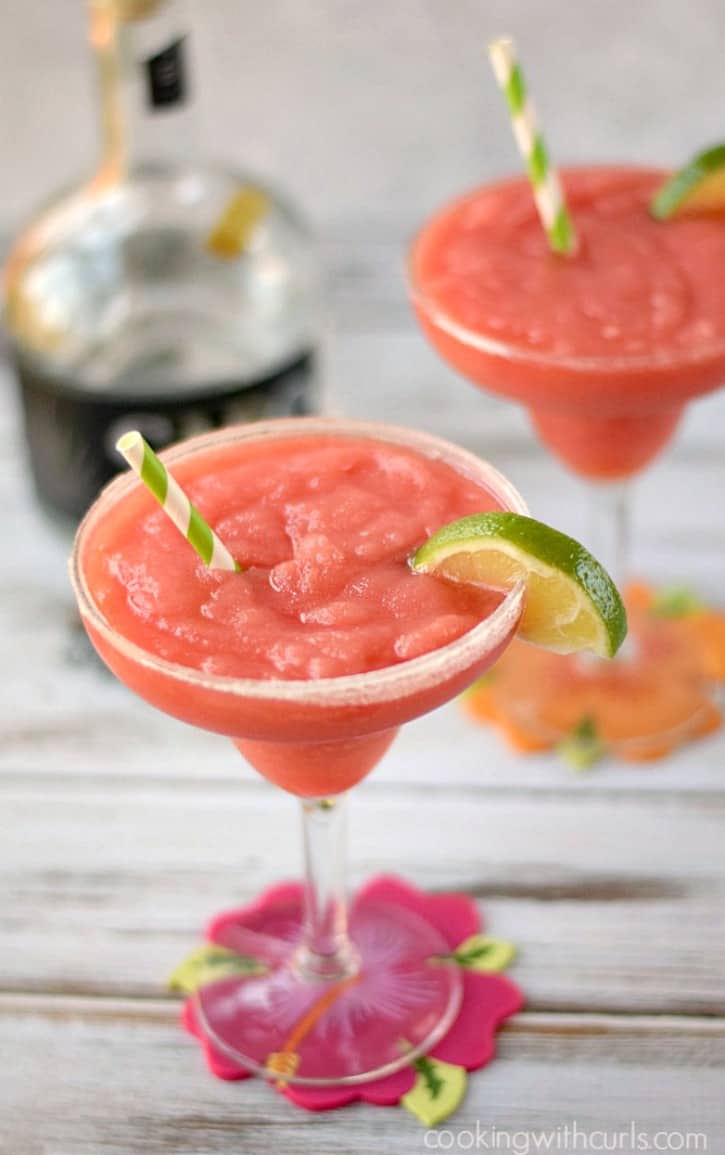 Two Frozen Watermelon Margaritas garnished with a sugar rimmed glass, lime slices and green and white striped straws. 