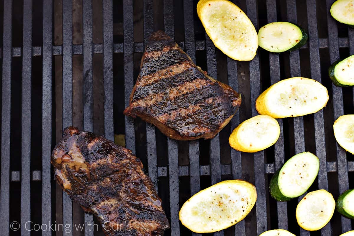 Two steaks on the grill with sliced squash on the side. 