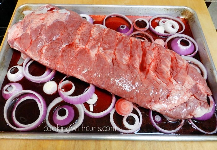 baking sheet with onion slices and wine with a rack of ribs on top