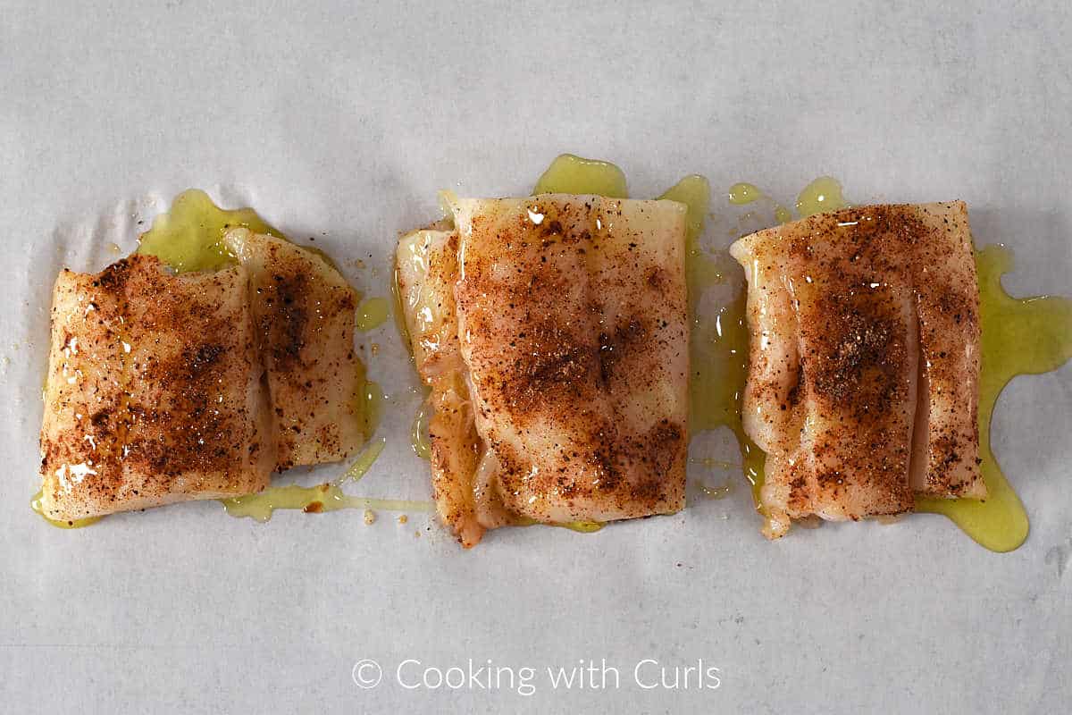 three-seasoned-pieces-of-cod-drizzled-with-oil-on-a-baking-sheet-with-parchment-paper.