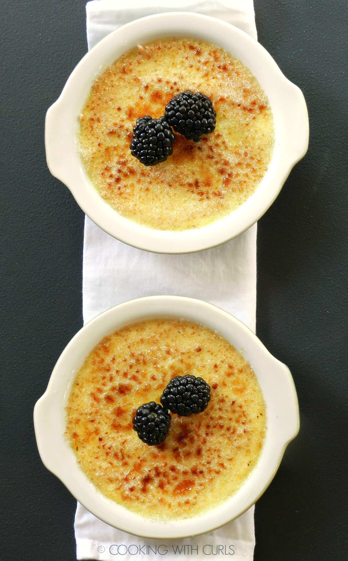 Looking down on two Creme Brulee topped with caramelized sugar and blackberries. 