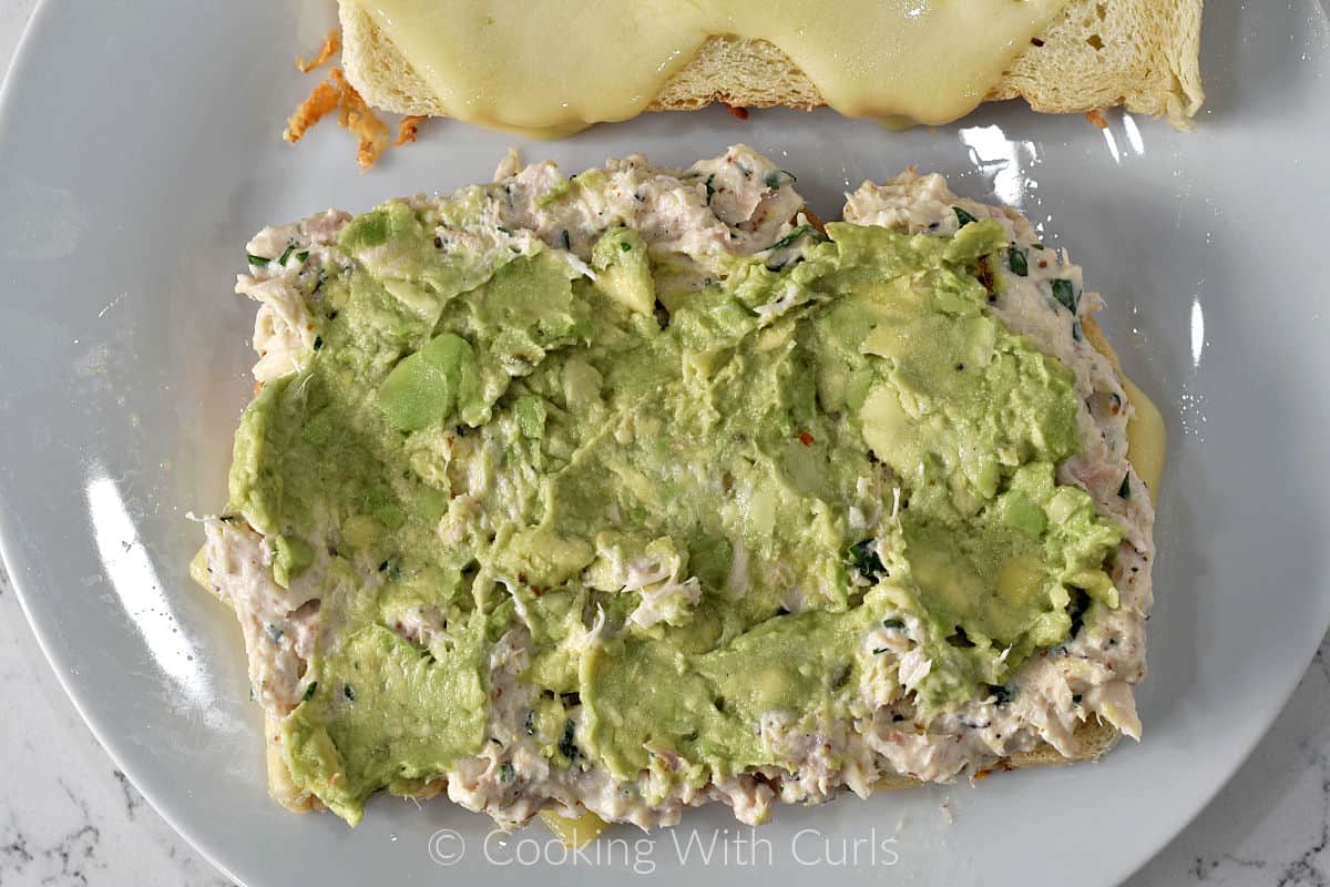 Mashed avocado on top of tuna salad on a slice of sourdough bread. 
