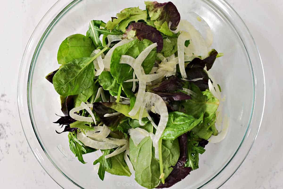 Shaved fennel and mixed greens in a glass bowl.