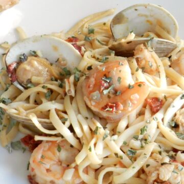 A large white plate with shrimp, clams and noodles in a garlic sauce.