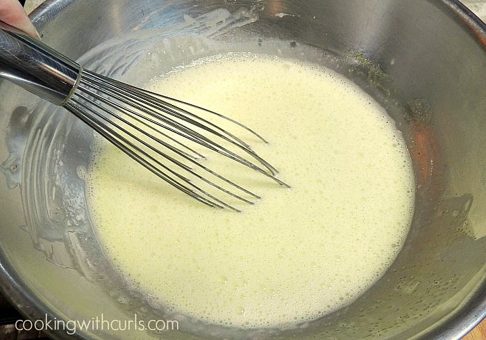 The hot coconut milk being whisked into the egg mixture in a stainless steel bowl. 