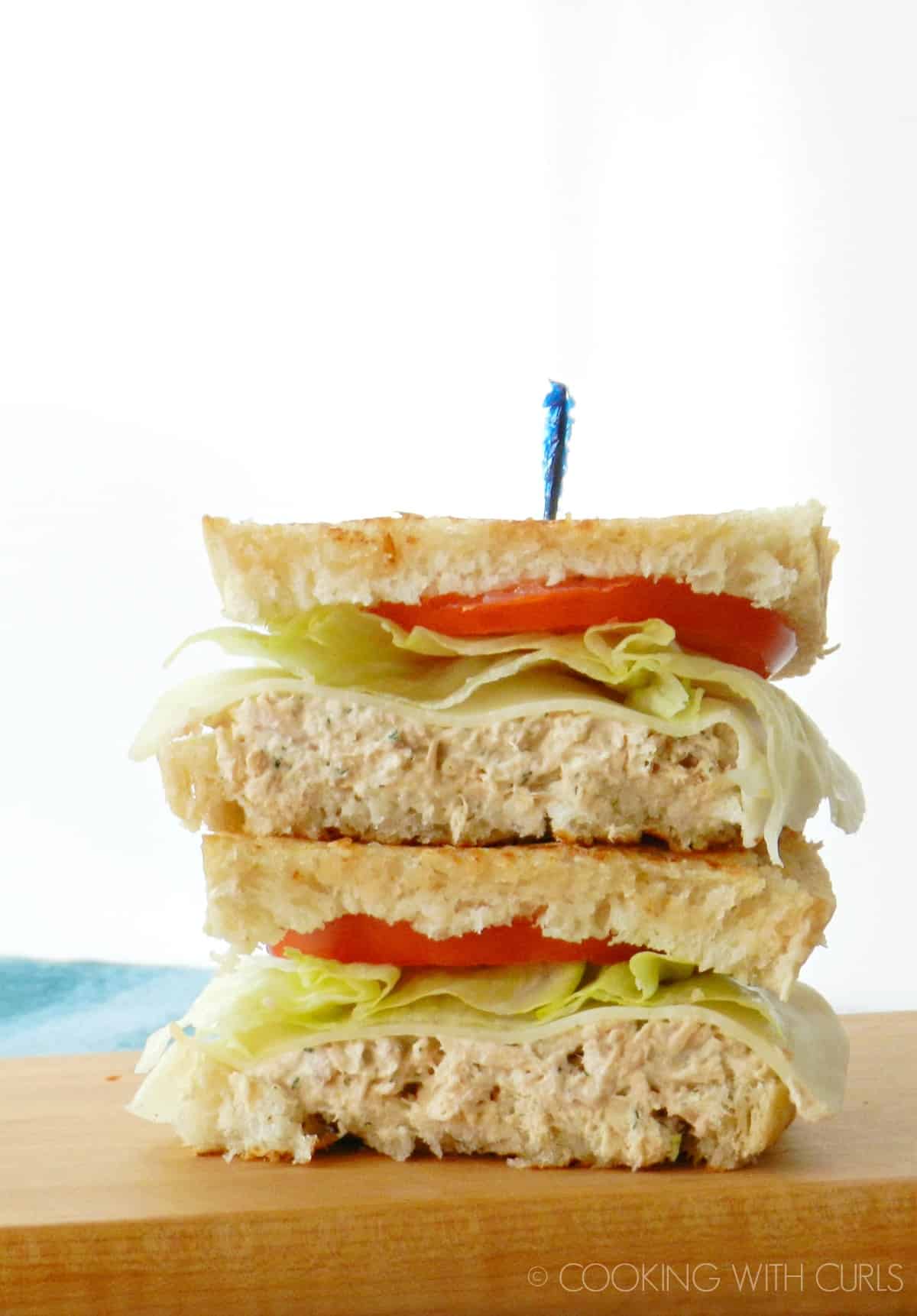 Tuna salad on Grilled Sourdough with provolone cheese, lettuce, and tomato slices cut in half and stacked.