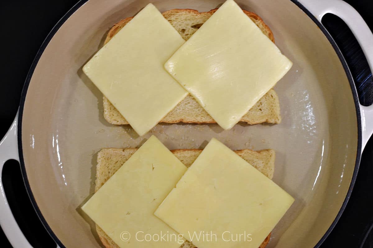 Two slices of sourdough bread topped with two slices of white cheese in a large skillet. 
