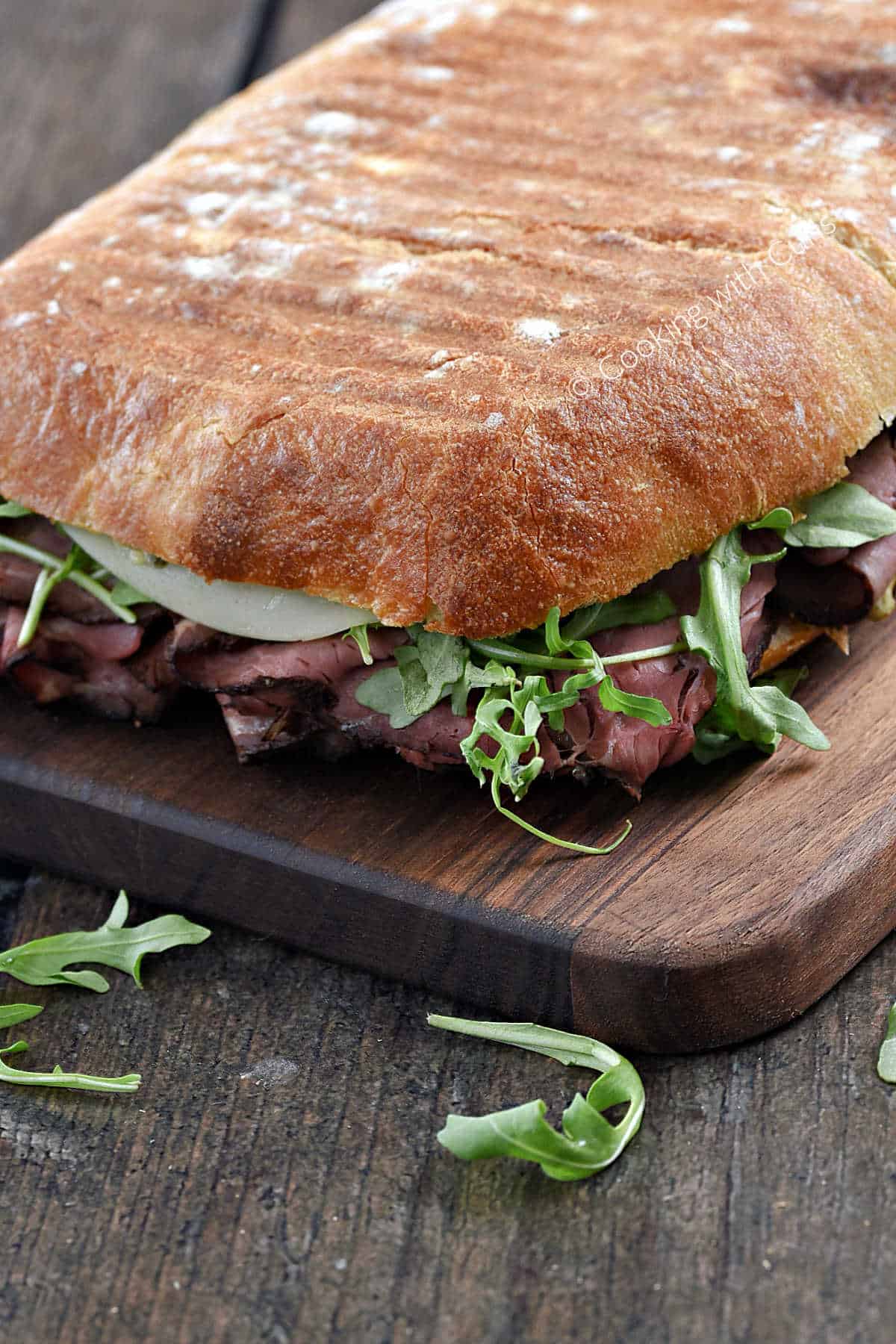 A grilled roast beef panini sandwich on a wooden serving board.