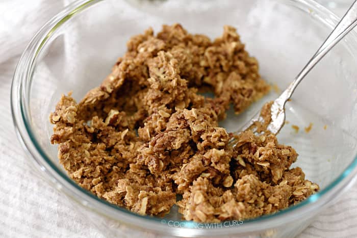 flour, oats, brown sugar, butter and pecans mixed together in a glass bowl with a fork. 