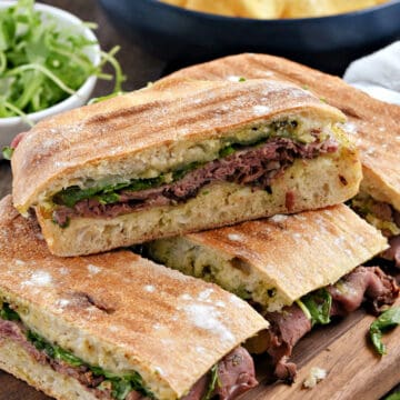 Roast beef panini sandwiches stacked on top of each other on a wooden board.