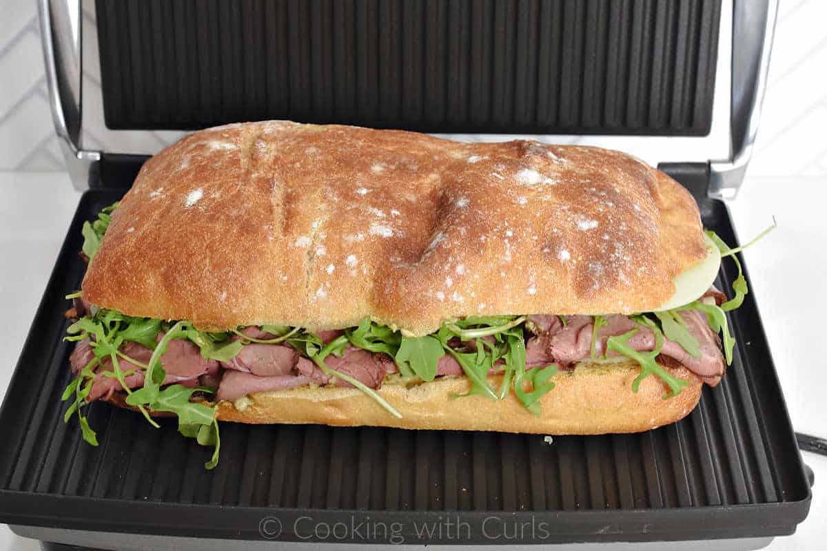 Roast beef sandwich on ciabatta bread inside a panini grill.