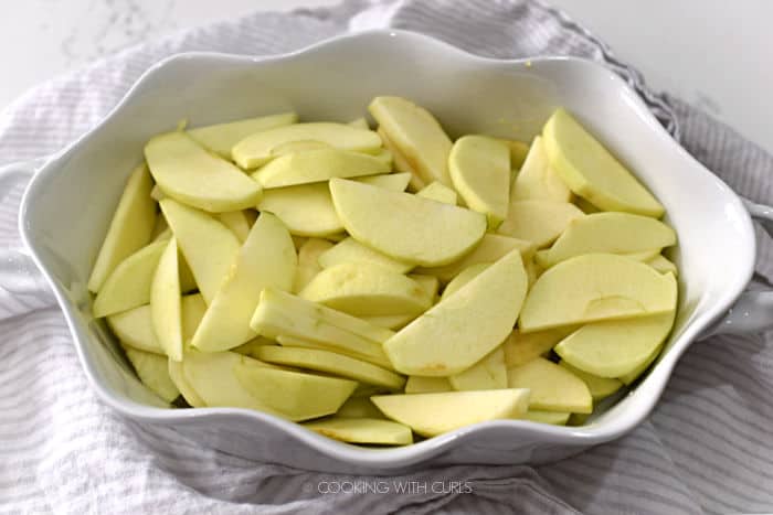 sliced apples layered in a white, curvy baking dish. 