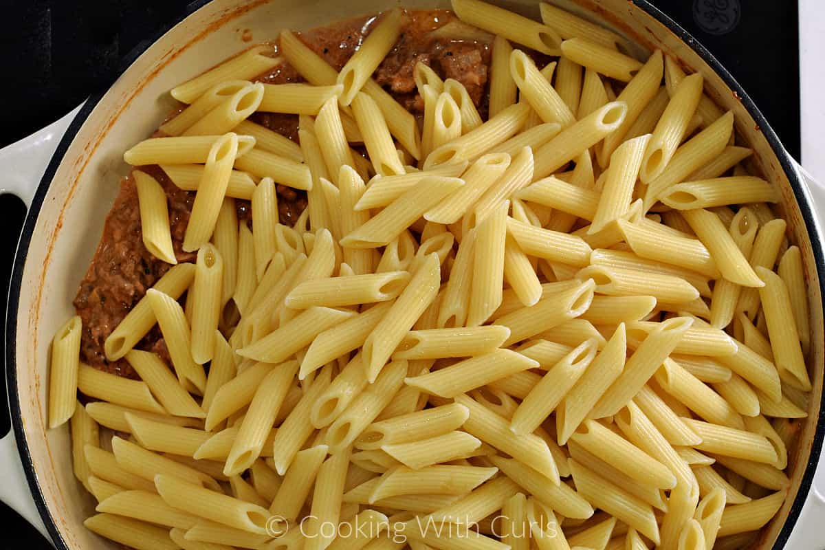 Cooked pasta on top of the cooked meat mixture in a large skillet. 
