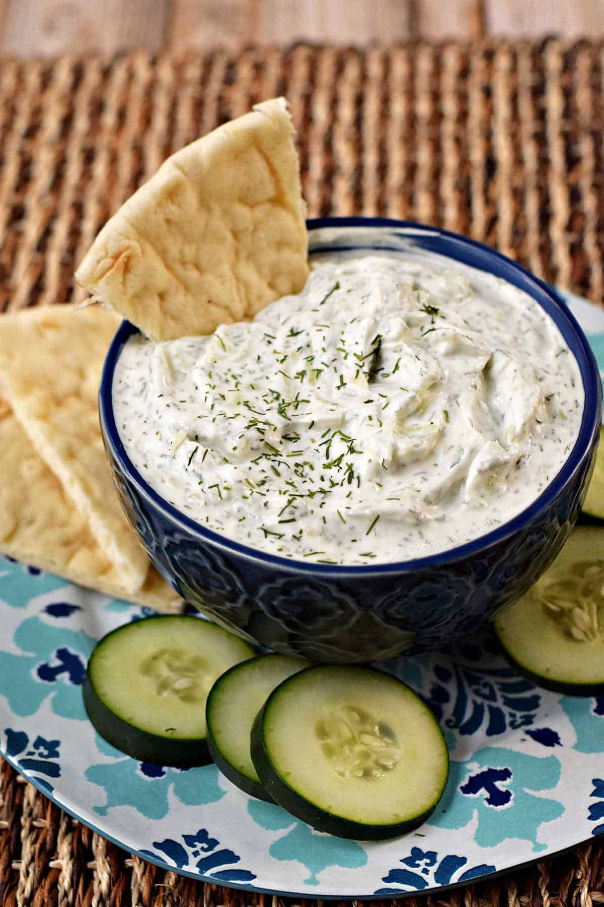 Cucumber and yogurt dip in a small bowl with pita chips and sliced cucumber.